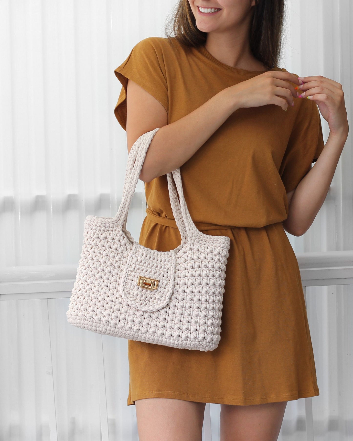 May include: A white crocheted tote bag with a gold clasp closure. The bag has a simple, casual design and is perfect for everyday use.