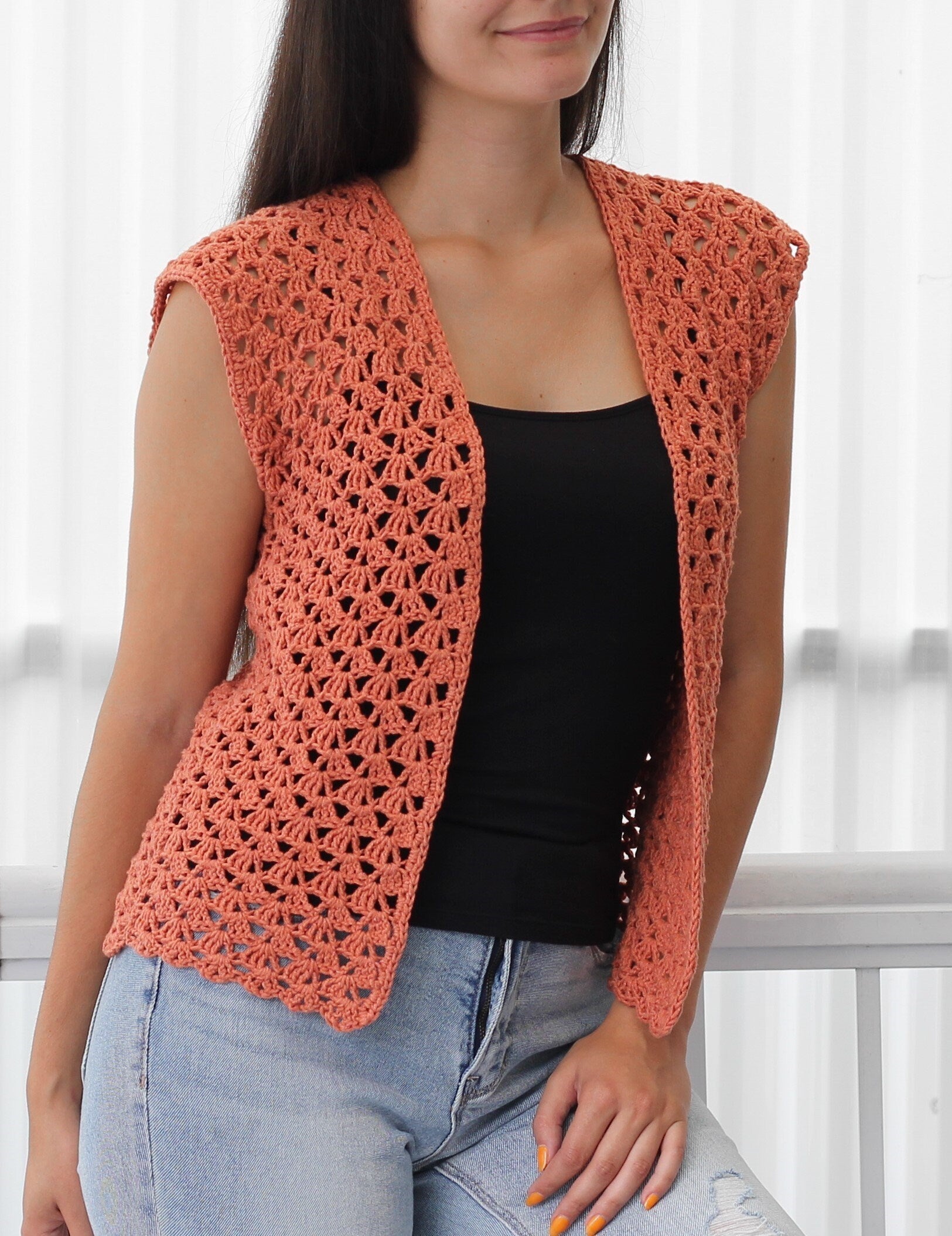 May include: A crocheted sleeveless vest in a peachy-coral color. The vest has a V-neck and a delicate open stitch pattern.