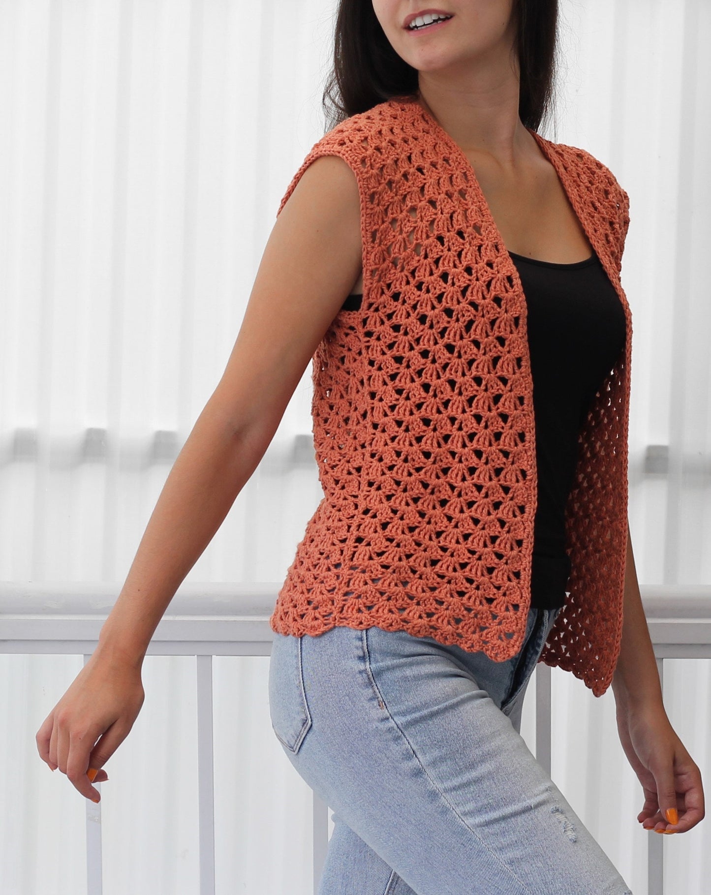 May include: A crocheted sleeveless vest in a coral color. The vest has a V-neck and a scalloped hem.