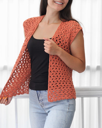 May include: A crocheted sleeveless vest in a terracotta color. The vest has a delicate openwork pattern and a V-neckline.