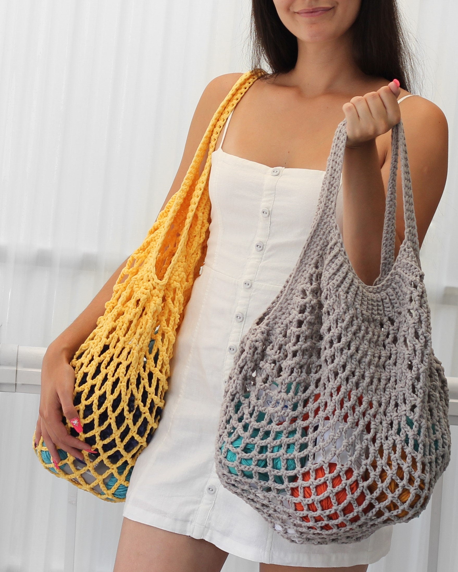 May include: Two crocheted mesh bags, one yellow and one gray, with colorful yarn inside. The bags are being held by a person wearing a white dress.
