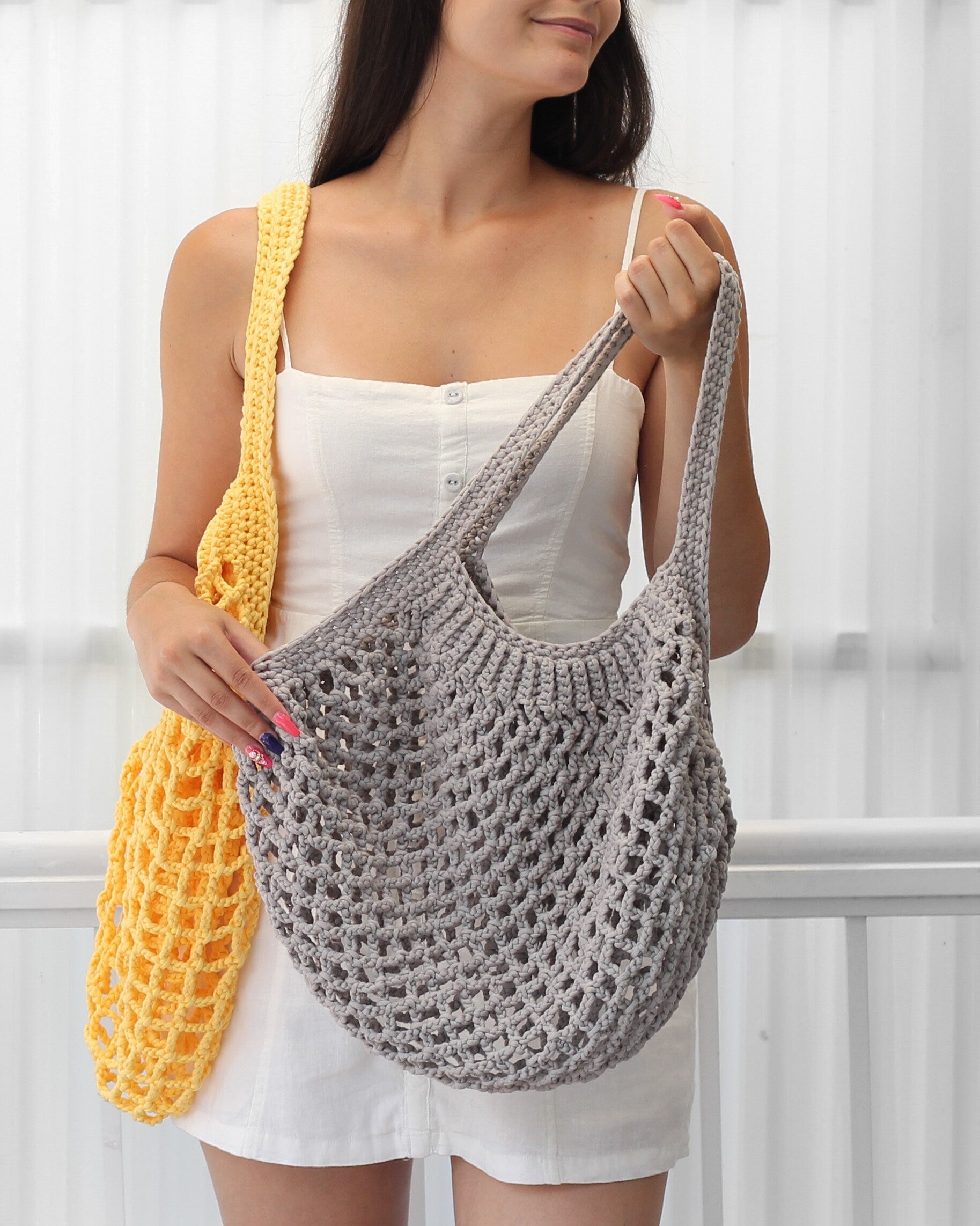 May include: Two crocheted tote bags, one yellow and one gray. The gray bag is being held by a person wearing a white tank top.