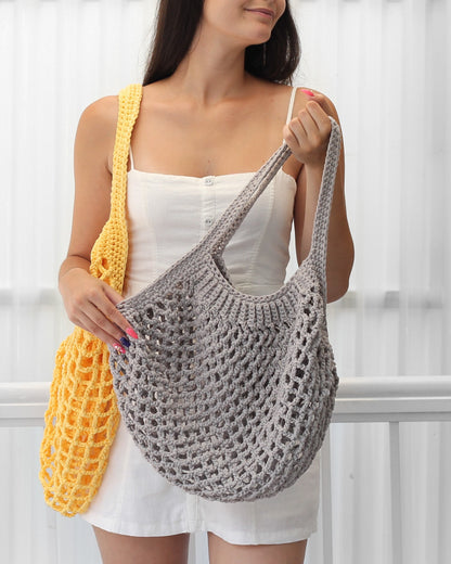 May include: Two crocheted tote bags, one yellow and one gray. The gray bag is being held by a person wearing a white tank top.