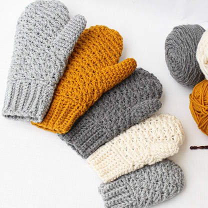 May include: Five crocheted mittens in various colors, including gray, white, and yellow. The mittens are arranged in a semi-circle on a white surface.