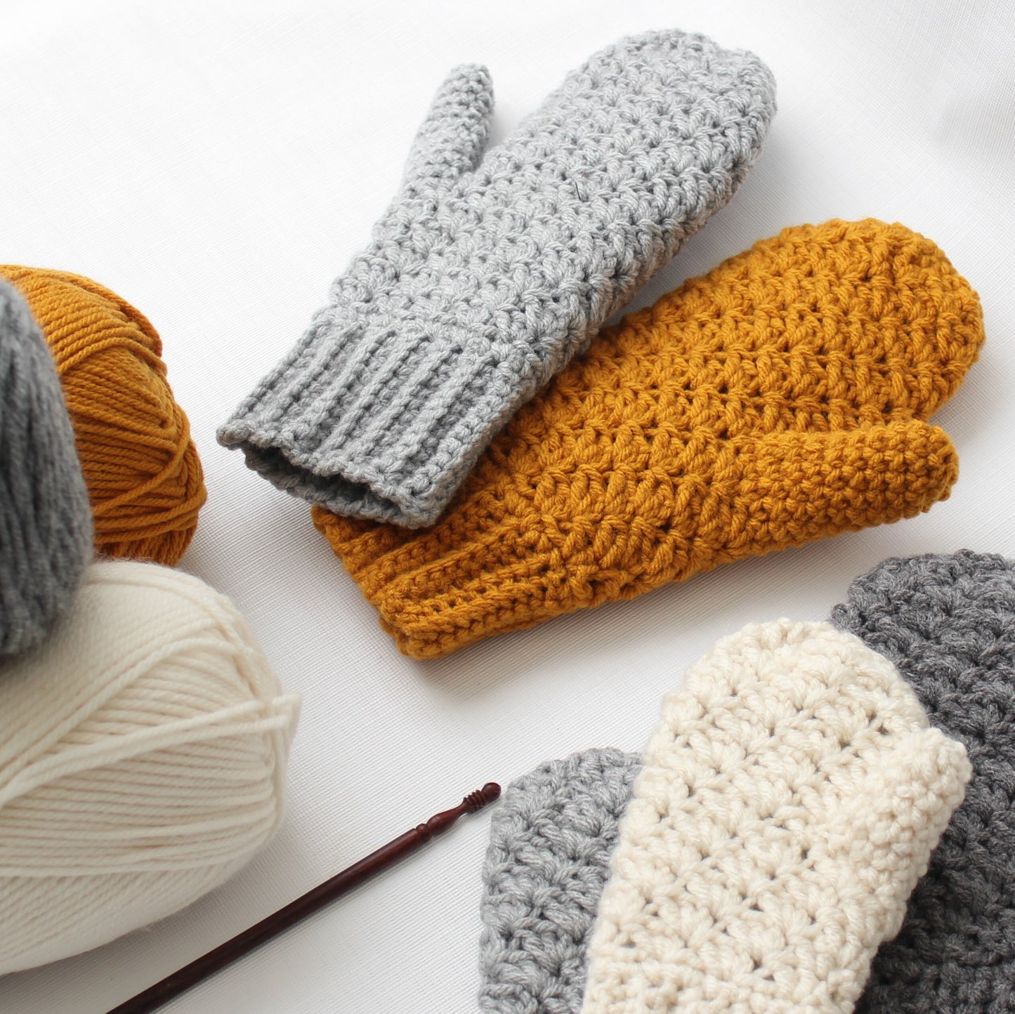 May include: A set of four crocheted mittens in gray, beige, and mustard yellow. The mittens are made with a textured stitch and are perfect for keeping your hands warm in the winter.