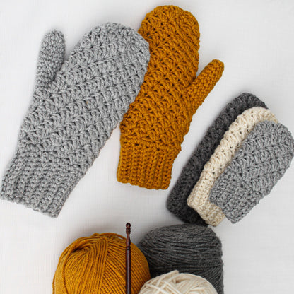May include: A set of crocheted mittens in gray, white, and mustard yellow. The mittens are arranged on a white surface with balls of yarn in the same colors.