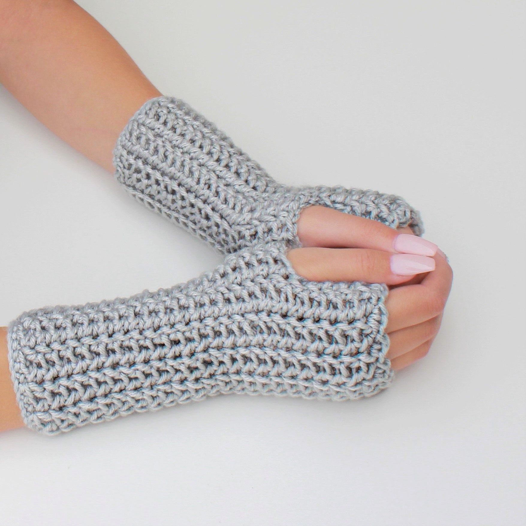 May include: A pair of gray fingerless gloves made of crocheted yarn. The gloves are shown on a person's hands.