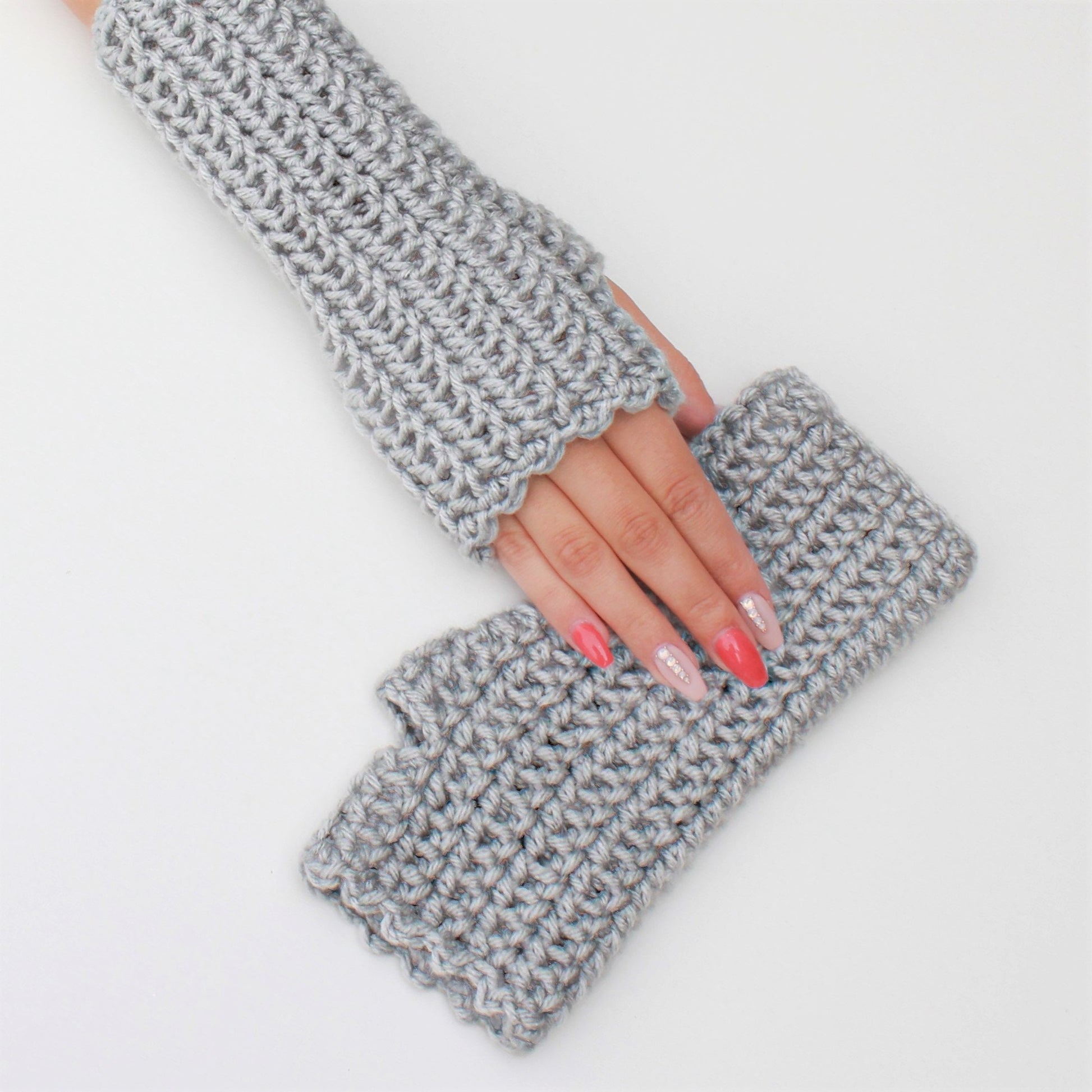 May include: A pair of gray fingerless gloves made of crocheted yarn. The gloves have a scalloped edge and are shown folded in half.