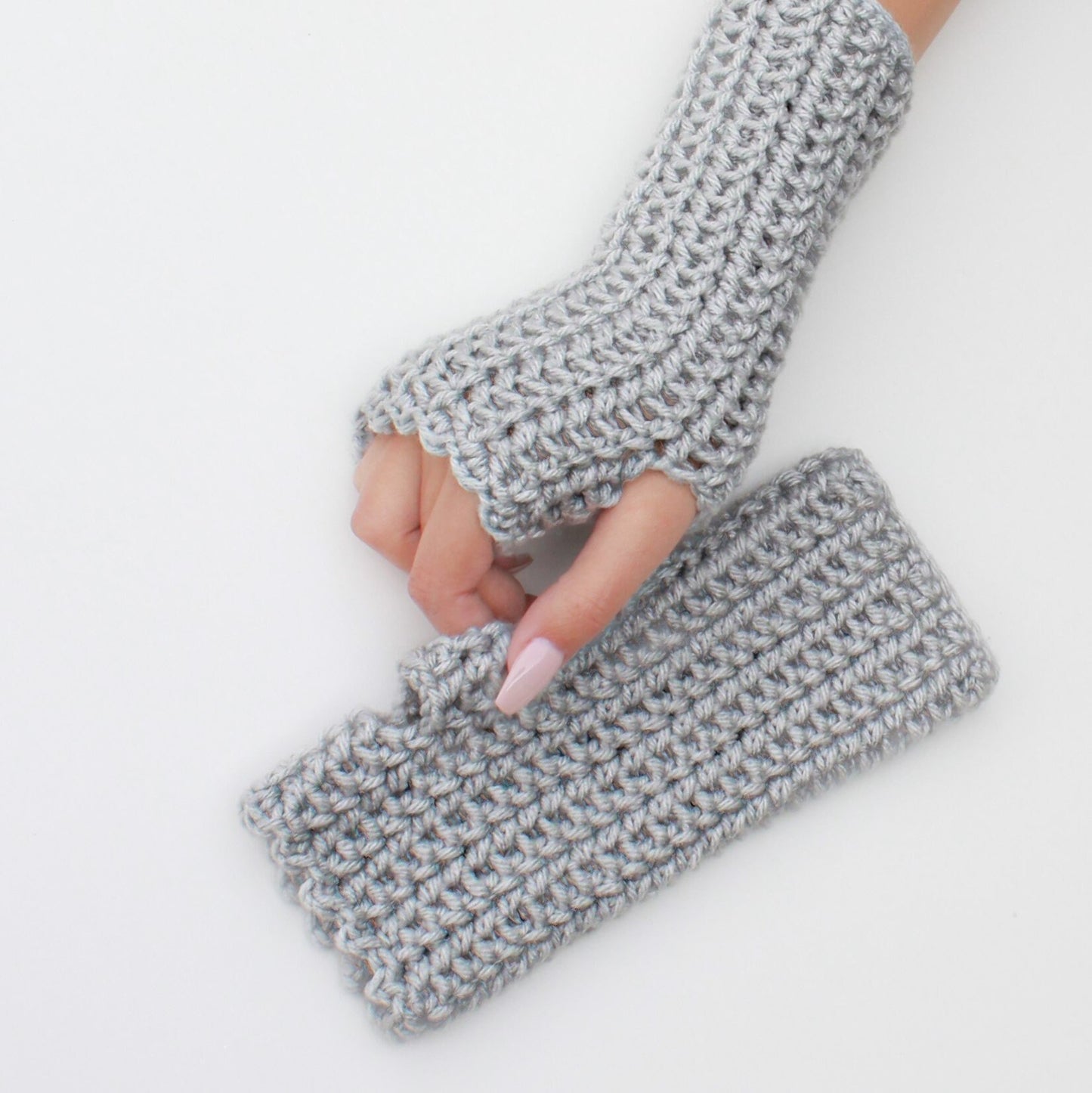 May include: A pair of gray fingerless gloves made of crocheted yarn. The gloves are laid flat on a white surface.