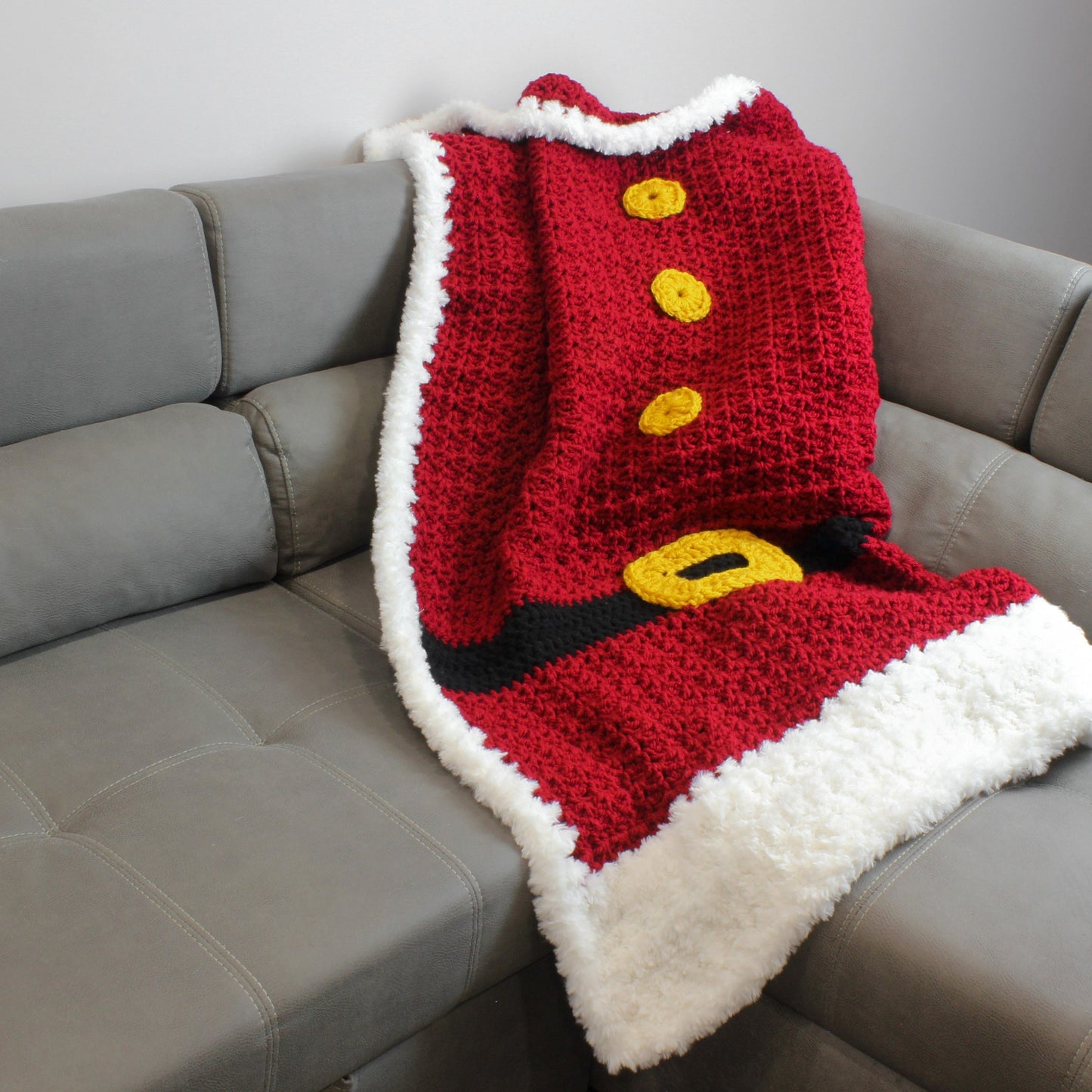 May include: A red and white crocheted blanket with a black belt and yellow buttons, resembling a Santa Claus suit.
