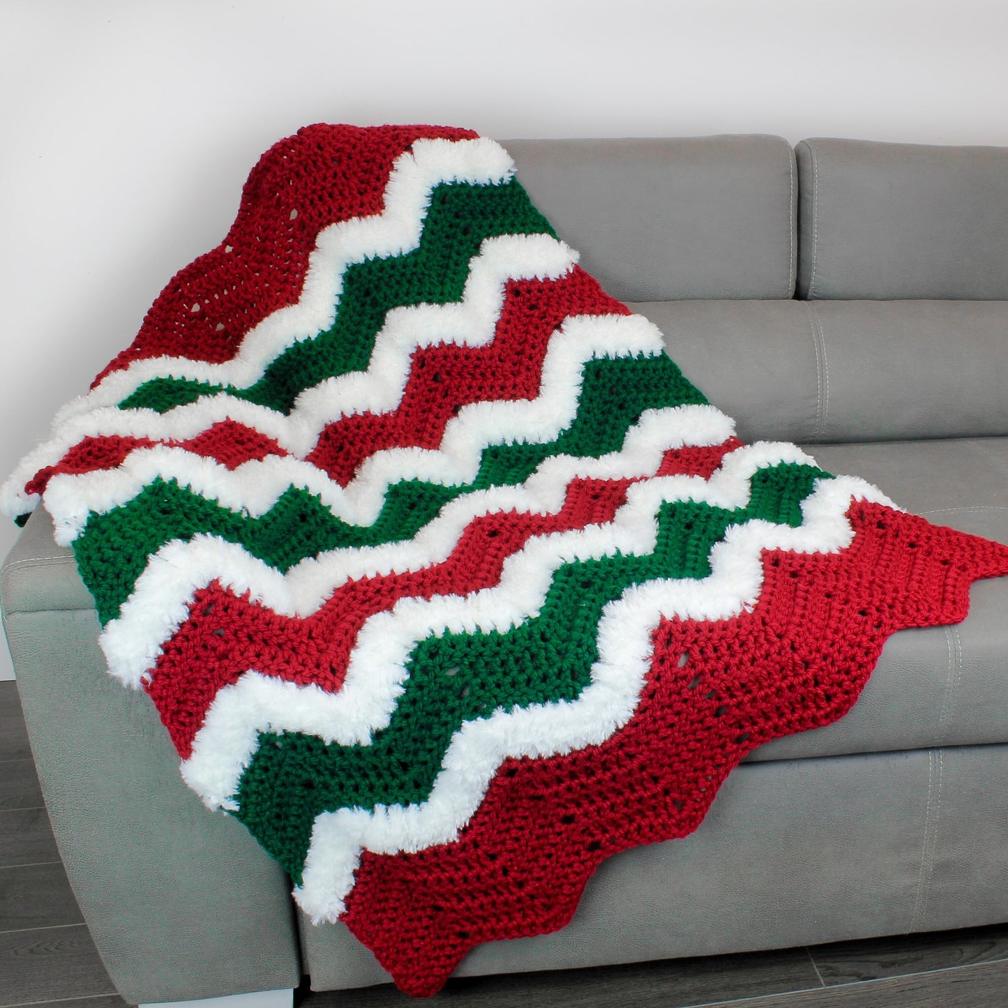 May include: A red, green, and white crocheted throw blanket with a chevron pattern. The blanket is draped over a gray couch.