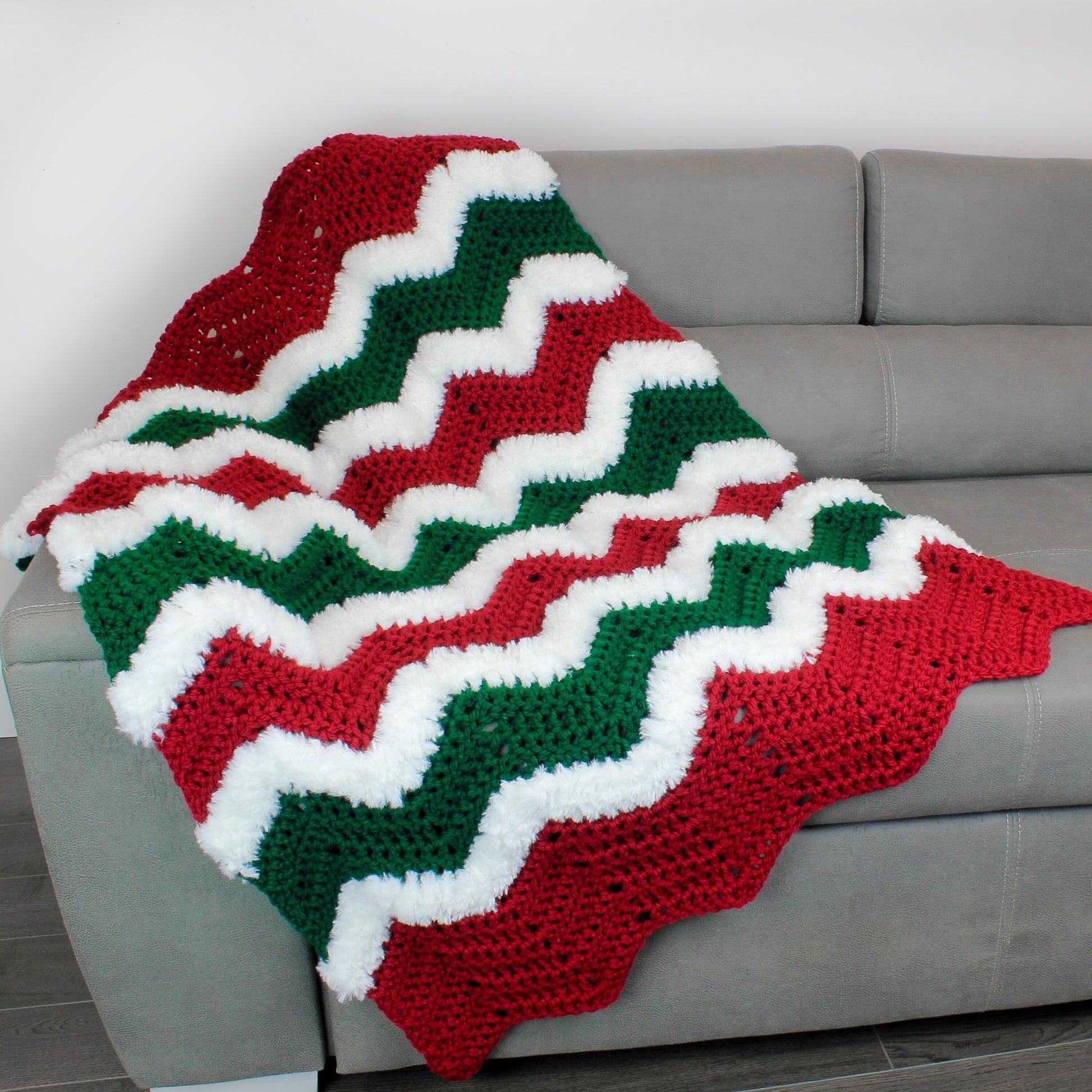 May include: A red, green, and white crocheted throw blanket with a chevron pattern. The blanket is draped over a gray couch.