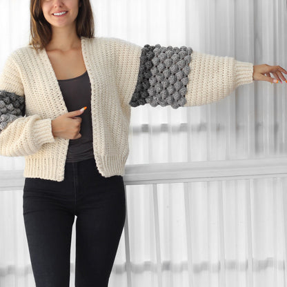 May include: A cream-colored crocheted cardigan with grey and white bobble stitch detailing on the sleeves.