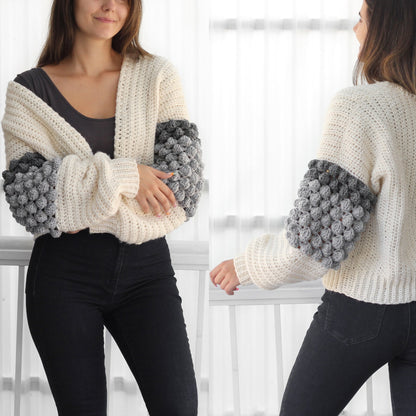 May include: A white crocheted cardigan with grey bobble stitch detailing on the sleeves. The cardigan is open in the front and has a relaxed fit.