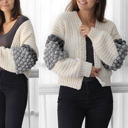 May include: A white crocheted cardigan with grey bobble stitch detailing on the sleeves. The cardigan has a V-neck and is cropped.