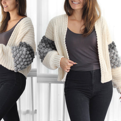 May include: A white crocheted cardigan with grey bobble stitch detailing on the sleeves. The cardigan is open in the front and has a V-neck.
