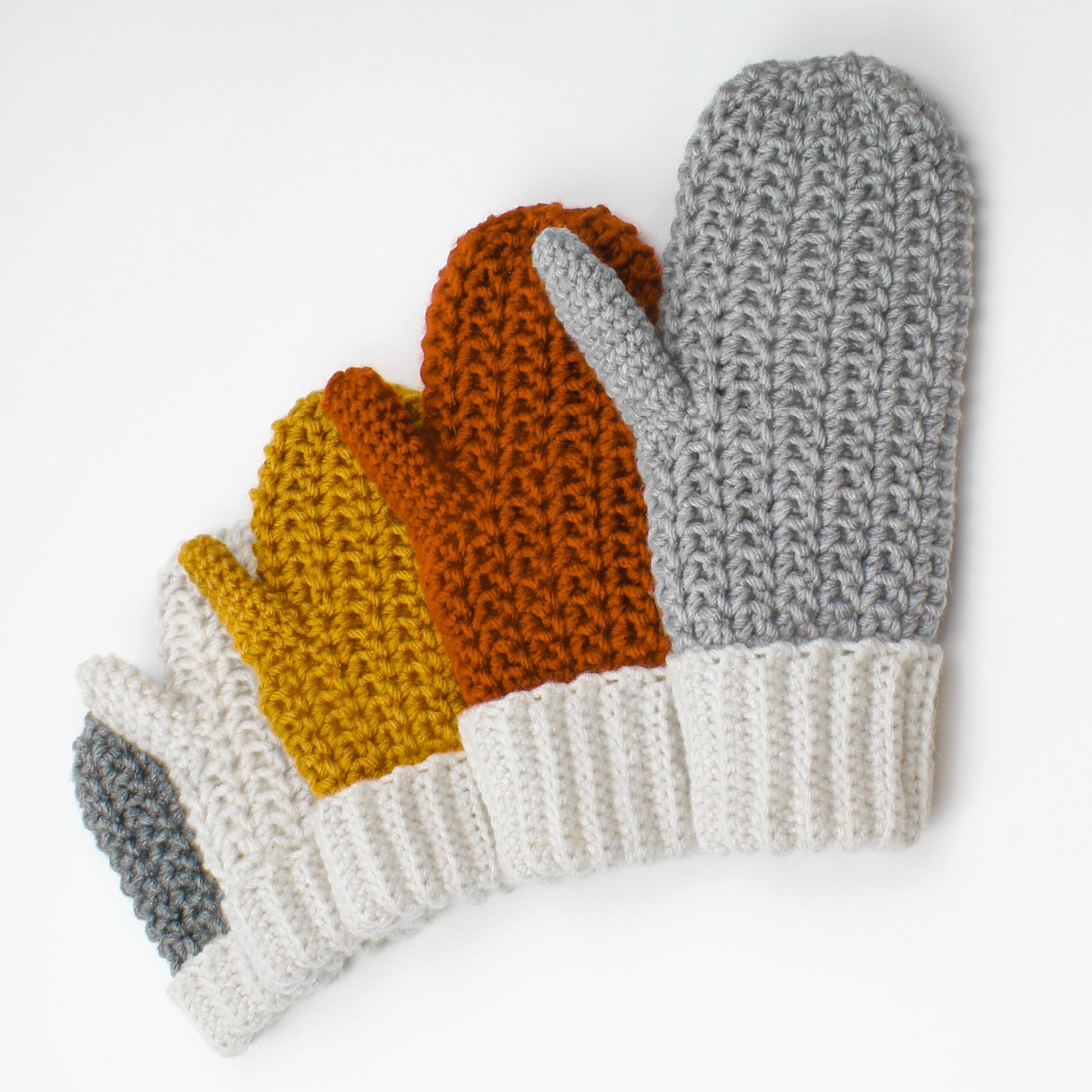 May include: Set of four crocheted mittens in gray, orange, yellow, and white. The mittens are arranged in a row, with the largest mitten on the right and the smallest mitten on the left.