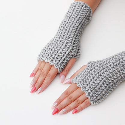 May include: A pair of gray fingerless gloves with a crocheted design. The gloves are worn on a person's hands, with pink nail polish on the fingernails.