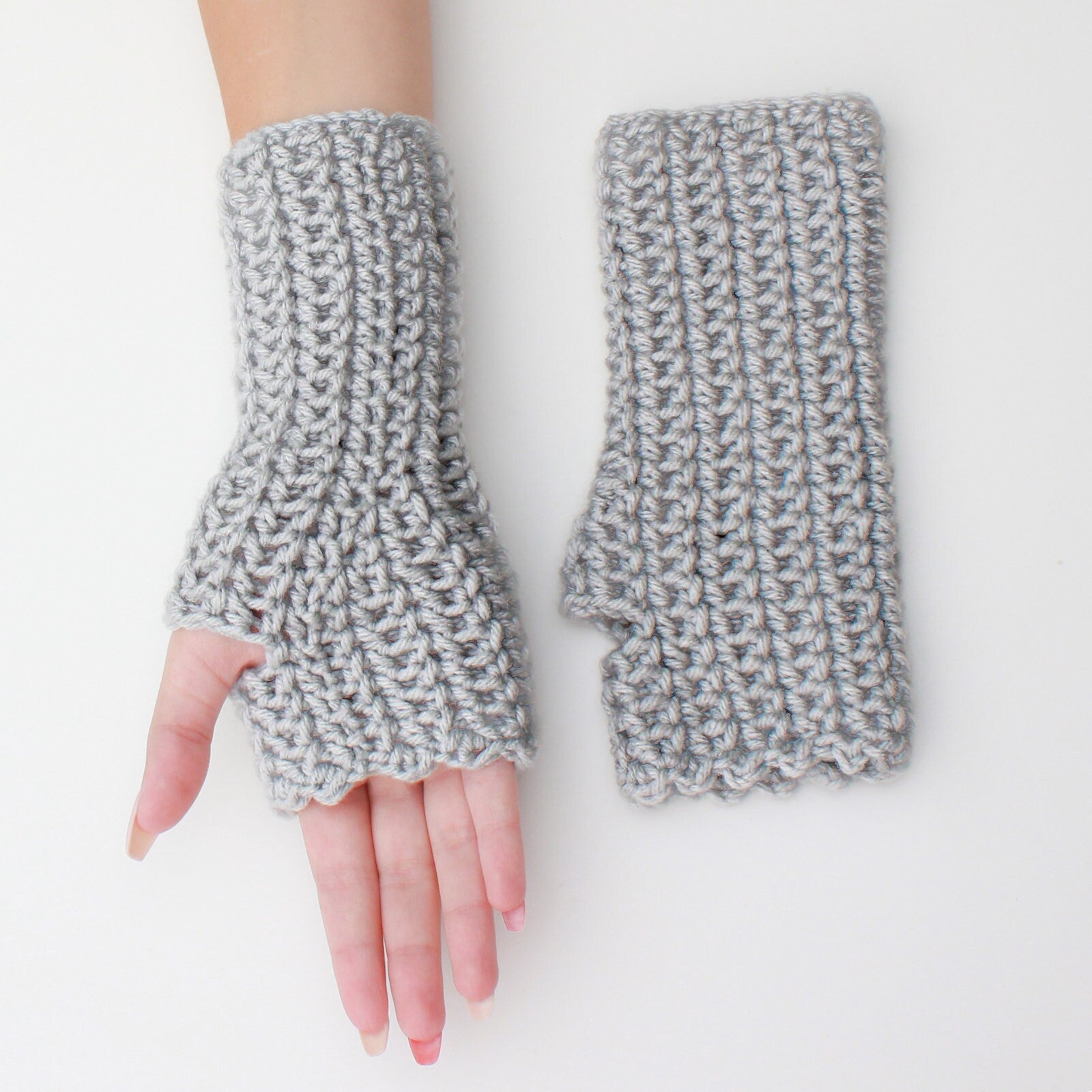 May include: A pair of gray fingerless gloves with a crocheted design. The gloves have a scalloped edge and a thumb hole.