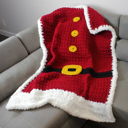 May include: A red crocheted blanket with a white border, designed to look like a Santa Claus suit. The blanket features a black belt with a yellow buckle and three yellow buttons.
