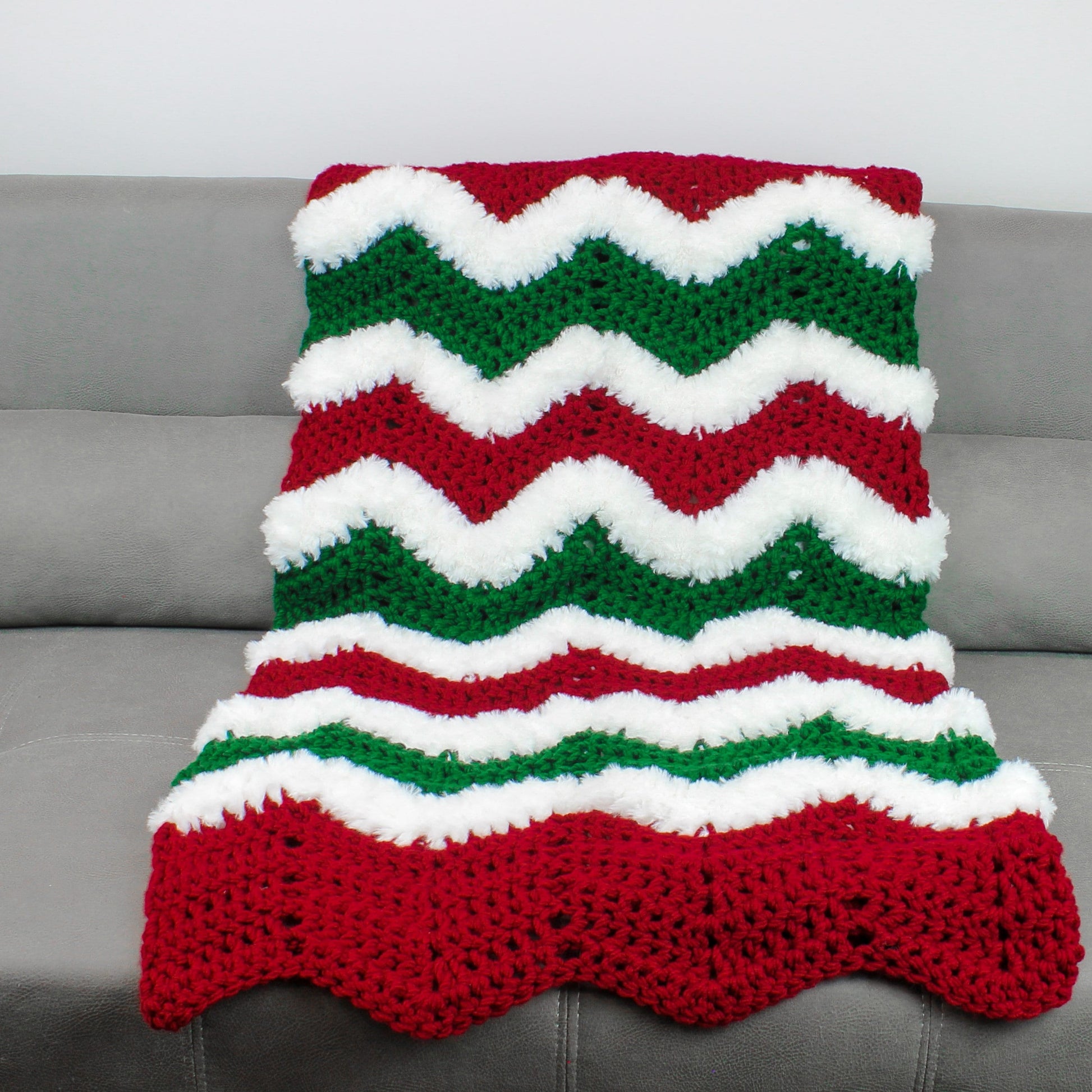 May include: A red, white, and green crocheted blanket with a chevron pattern. The blanket is made with fluffy yarn and has a scalloped edge.