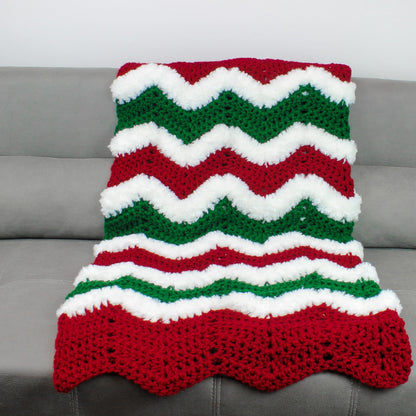 May include: A red, white, and green crocheted blanket with a chevron pattern. The blanket is made with fluffy yarn and has a scalloped edge.