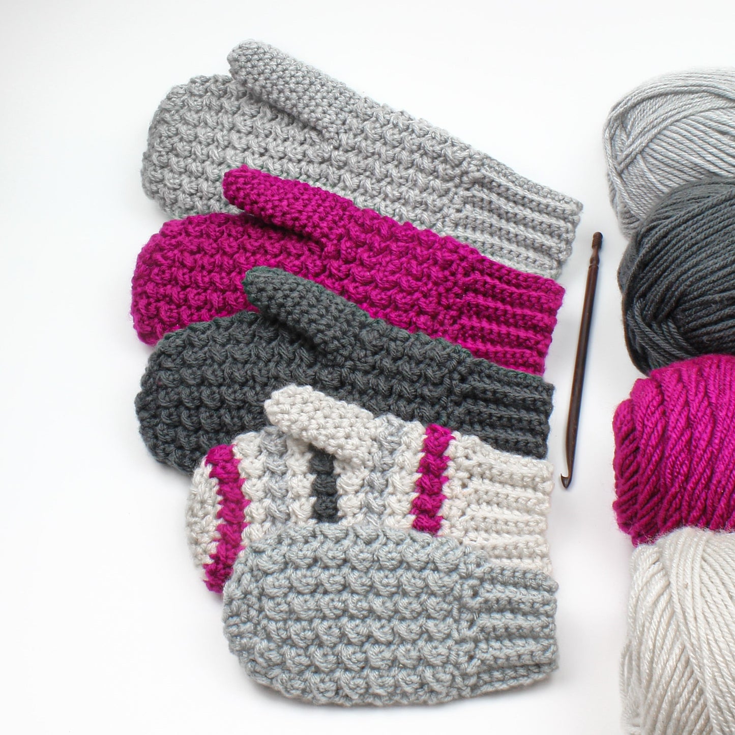 May include: A stack of crocheted mittens in gray, pink, and white. The mittens are arranged in a pyramid shape, with the largest mitten at the bottom and the smallest mitten at the top. The mittens are made with a textured stitch.