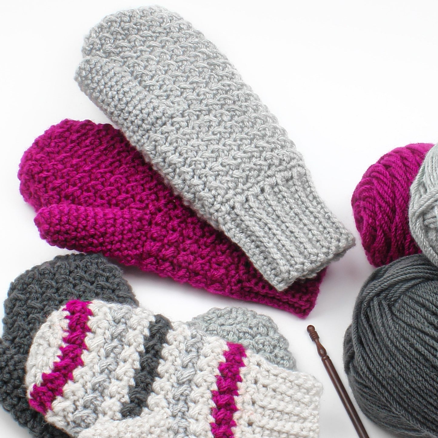 May include: Three pairs of crocheted mittens in gray, pink, and white with gray, pink, and black yarn balls.