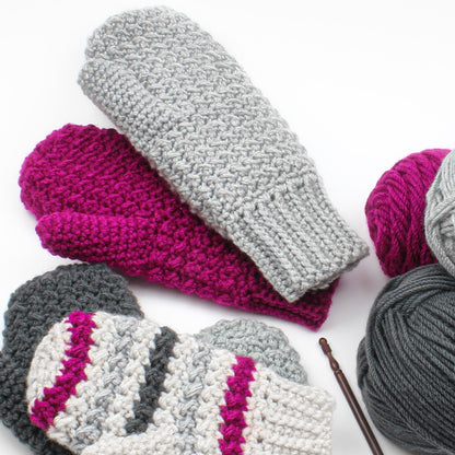 May include: Three pairs of crocheted mittens in gray, pink, and white with gray, pink, and black yarn balls.