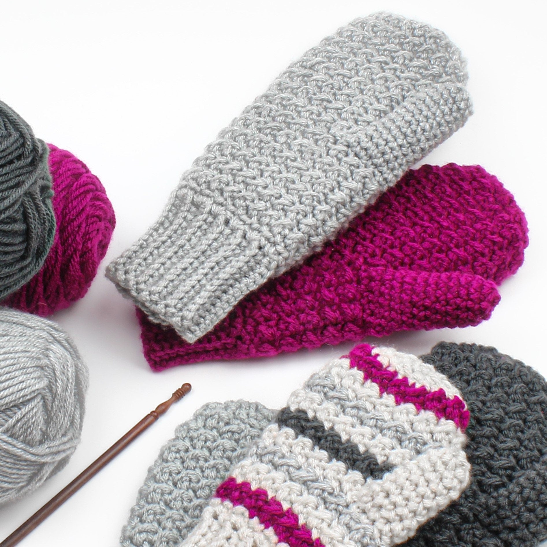 May include: Three pairs of crocheted mittens in gray and pink. The mittens are made with a textured stitch and have a striped pattern. The mittens are lying on a white surface.
