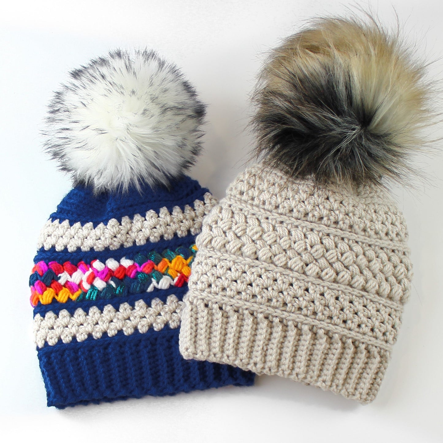 May include: Two crocheted winter hats with faux fur pom poms. One hat is blue with a colorful stripe and the other is beige.