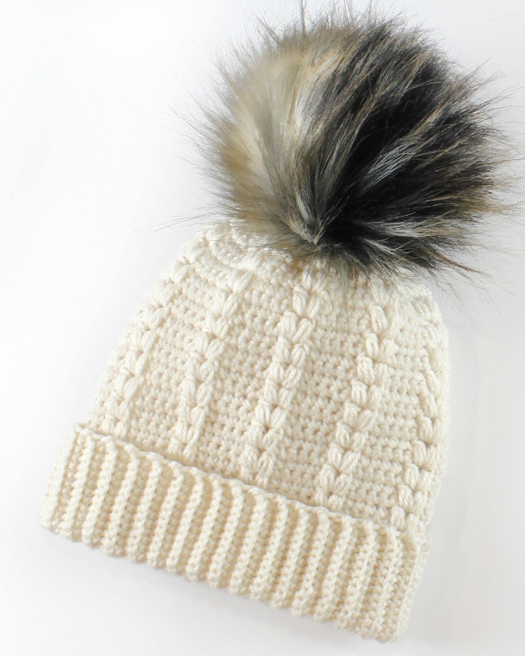 May include: A white crocheted beanie with a black and brown faux fur pom pom.