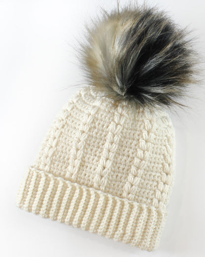 May include: A white crocheted beanie with a black and brown faux fur pom pom.