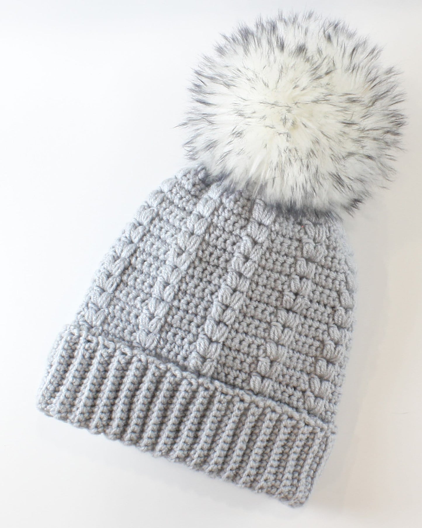 May include: A gray knitted beanie with a white faux fur pom pom on top.