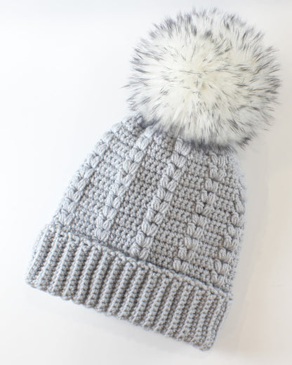 May include: A gray knitted beanie with a white faux fur pom pom on top.