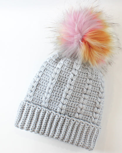 May include: A gray crocheted beanie with a fluffy pom pom in shades of pink, orange, and yellow.