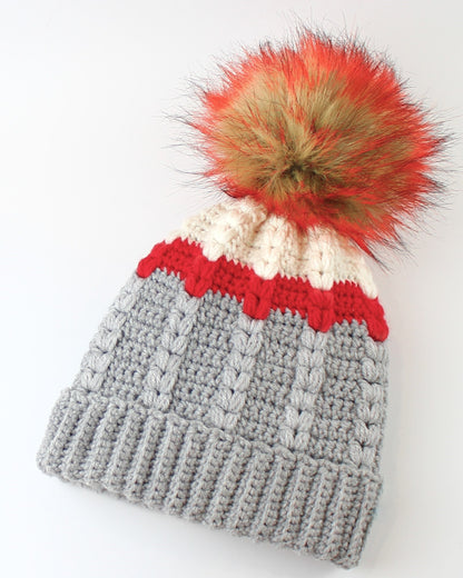 May include: Gray crocheted beanie with a red, white, and cream stripe pattern and a fluffy orange and brown pom pom.