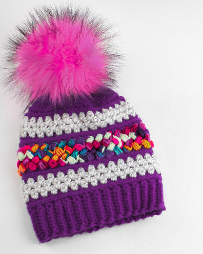 May include: Purple crochet beanie with a colorful braided stripe and a pink pom pom.