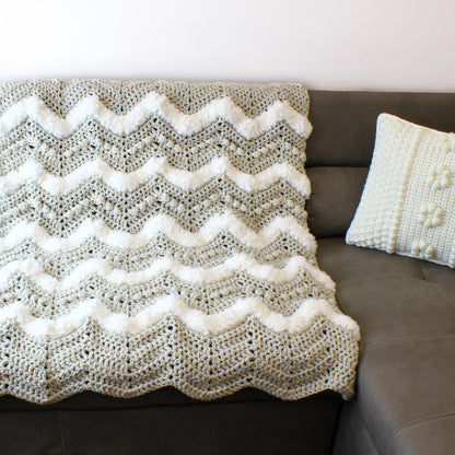 May include: A gray and white crocheted throw blanket with a chevron pattern. The blanket is draped over a brown couch.