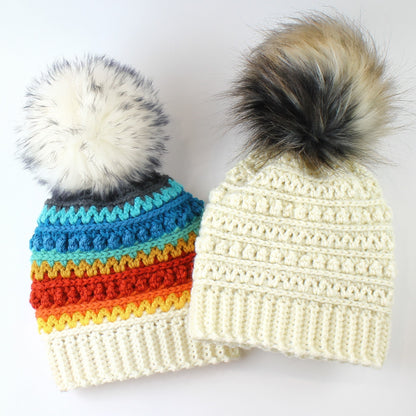 May include: Two crocheted hats with faux fur pom poms. One hat is white with a textured stitch and the other is white with a colorful striped pattern.