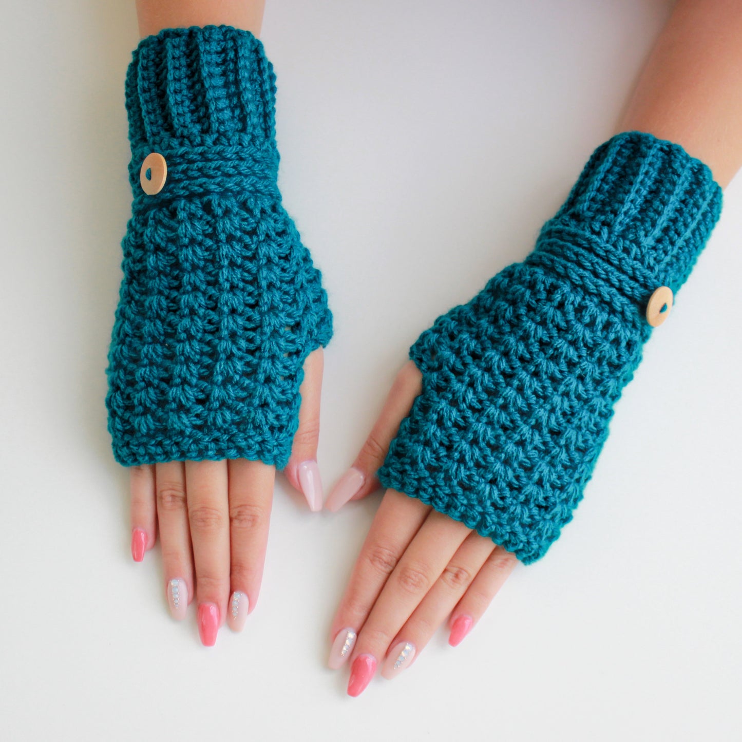 May include: A pair of teal blue fingerless gloves with wooden buttons. The gloves are crocheted and have a textured pattern.