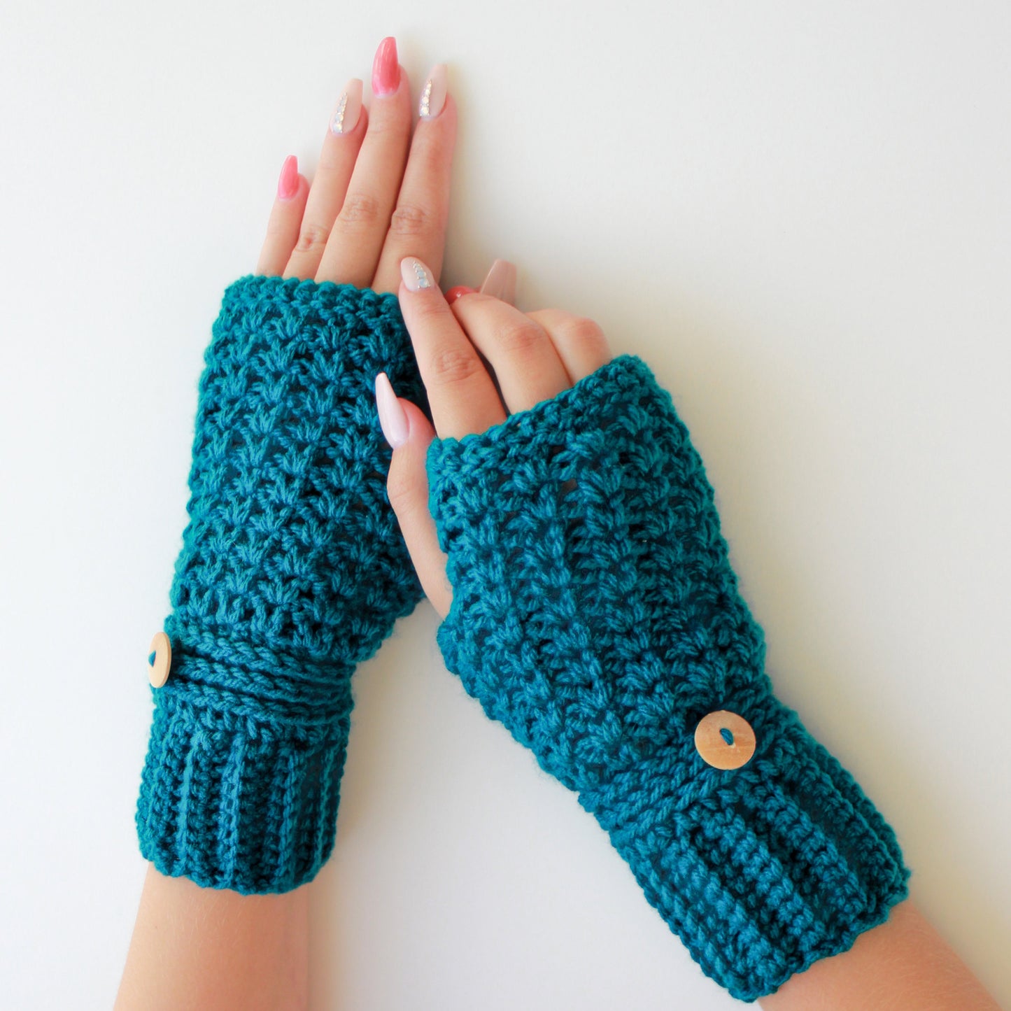May include: A pair of teal blue fingerless gloves with wooden buttons. The gloves are crocheted and have a textured pattern.