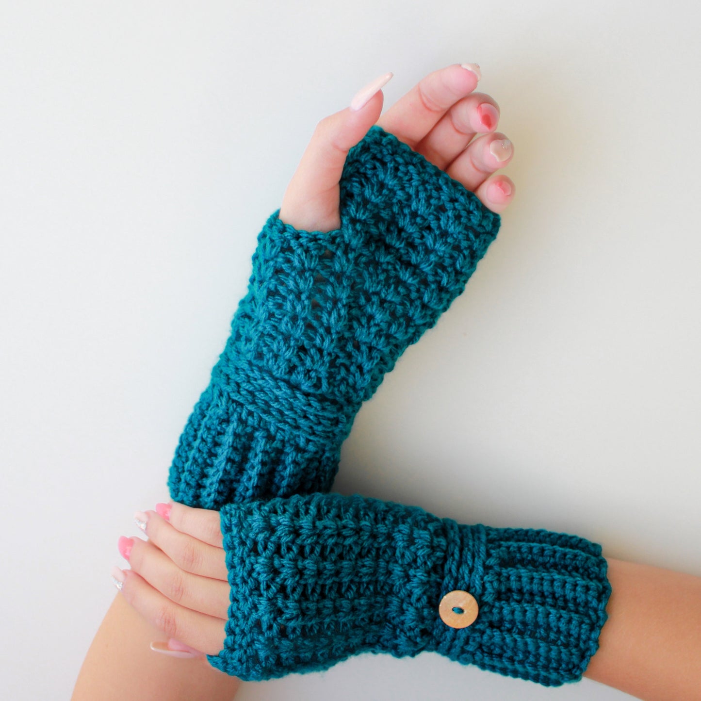 May include: A pair of teal blue crocheted fingerless gloves with a wooden button on one glove.