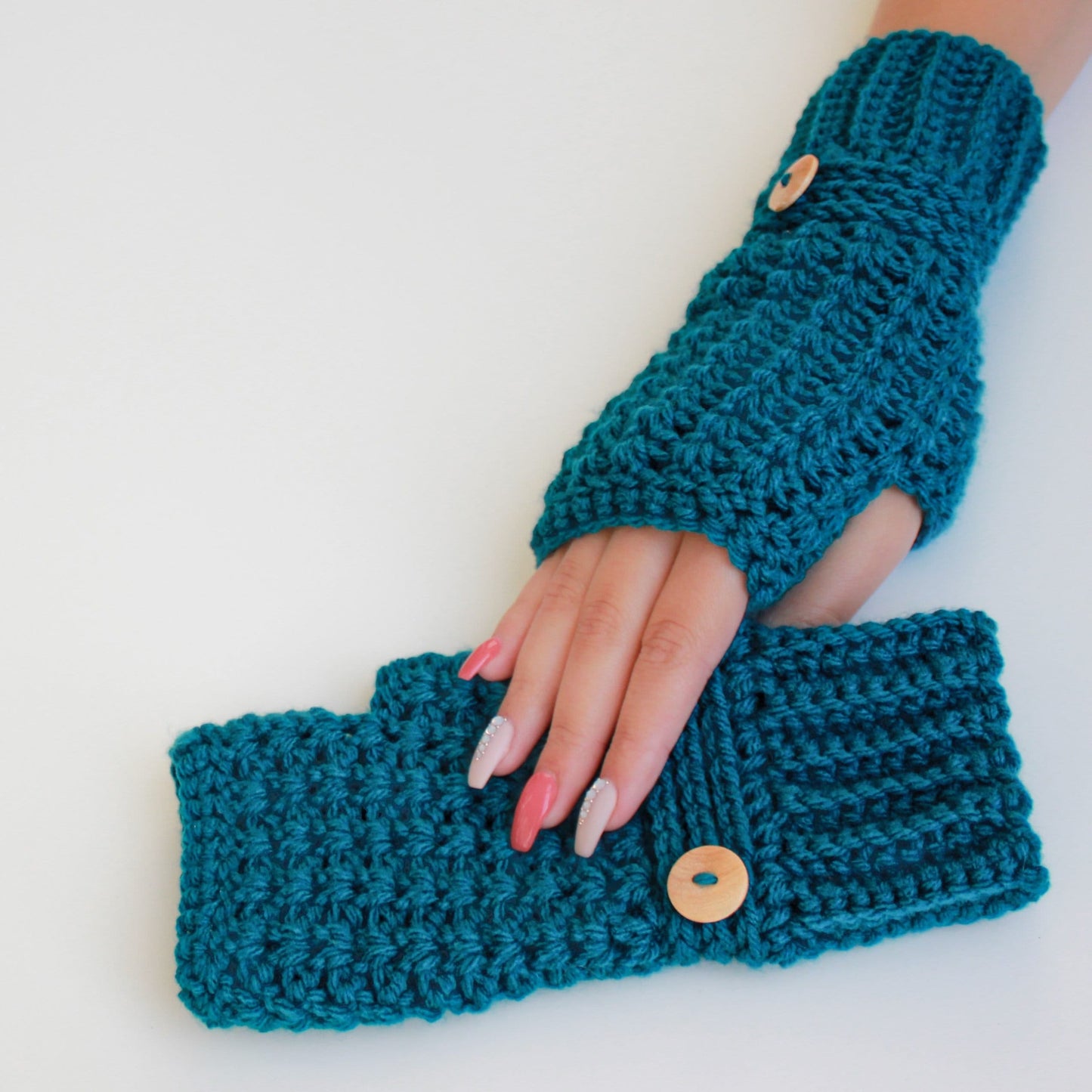 May include: Teal blue crocheted fingerless gloves with wooden buttons. The gloves are shown on a white background.