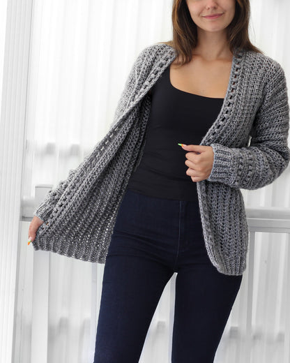 May include: A gray crocheted cardigan with a V-neck and long sleeves. The cardigan is open in the front and has a textured stitch pattern.