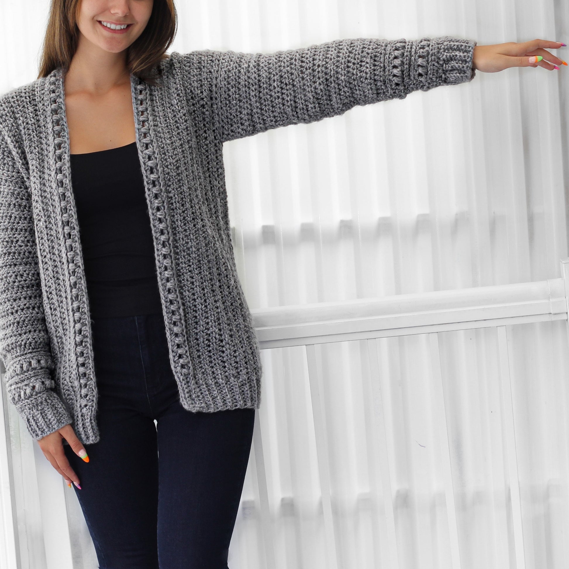 May include: A gray crocheted cardigan with a long sleeve and a v-neck. The cardigan has a textured stitch pattern and a ribbed trim.