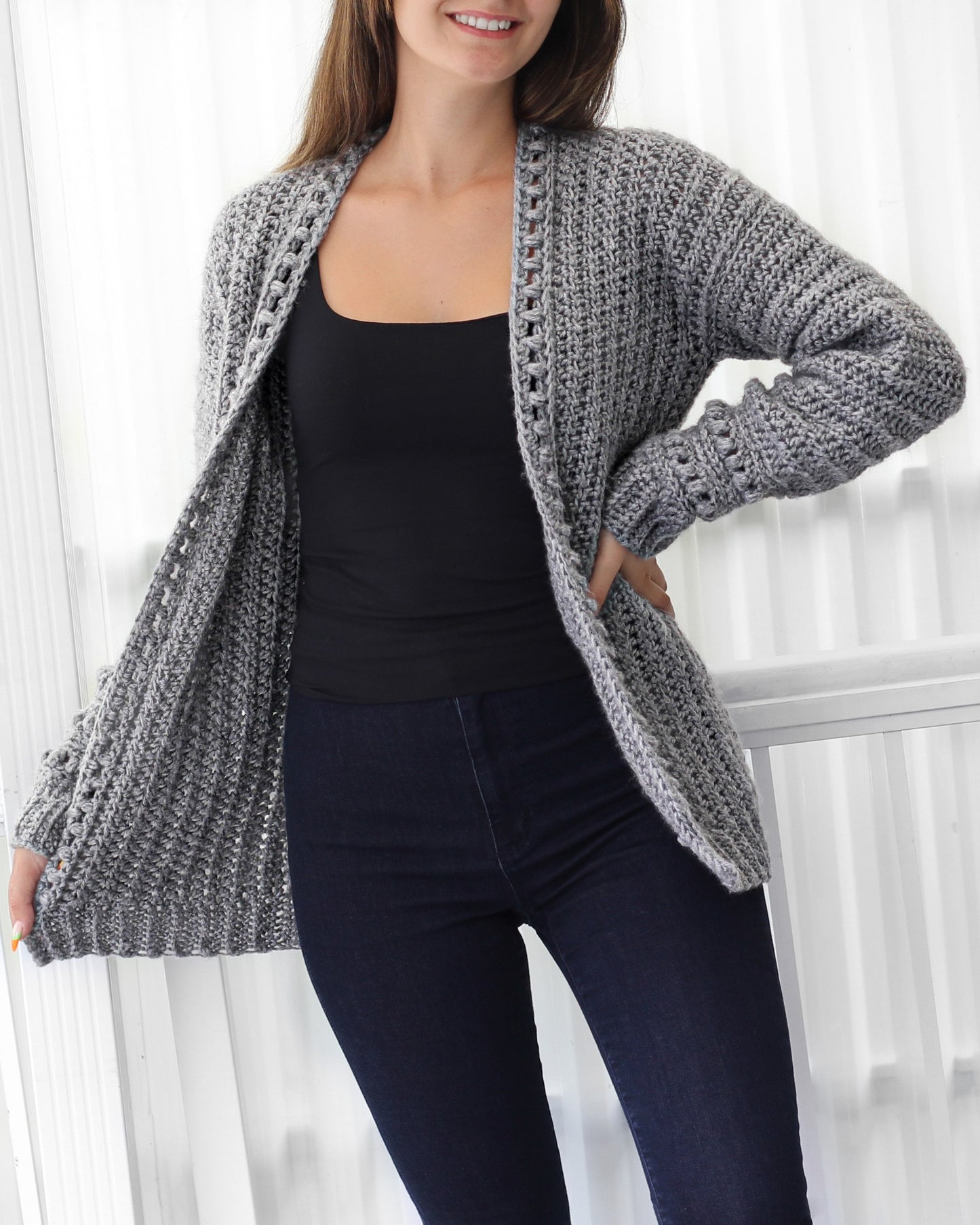May include: A gray crocheted cardigan with a ribbed texture and a crocheted trim around the neckline and cuffs. The cardigan is open in the front and has long sleeves.