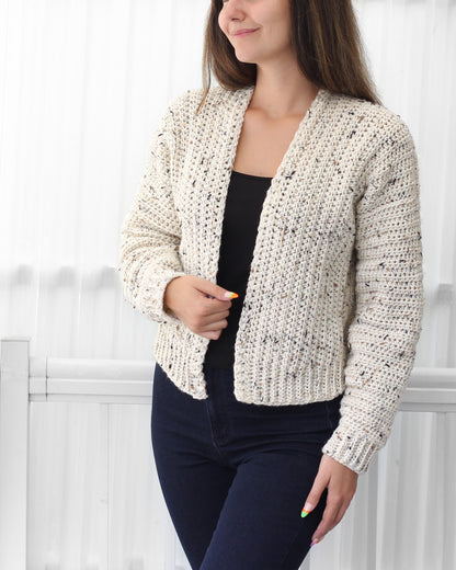 May include: A white crocheted cardigan with a speckled pattern. The cardigan has a V-neck and long sleeves.