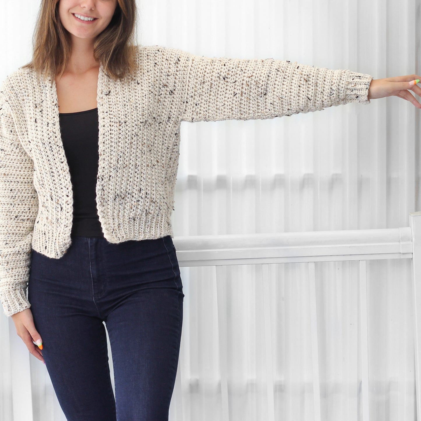 May include: A white crocheted cardigan with a speckled pattern. The cardigan has a V-neck and long sleeves.