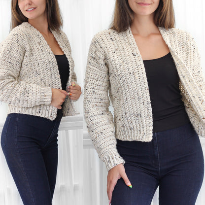 May include: A white crocheted cardigan with a speckled pattern. The cardigan has a V-neck and long sleeves. The model is wearing the cardigan with a black tank top and blue jeans.